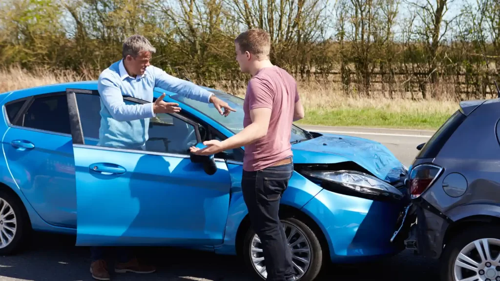 a man negotiating with insurance adjusters standing next to a blue car with a broken front end